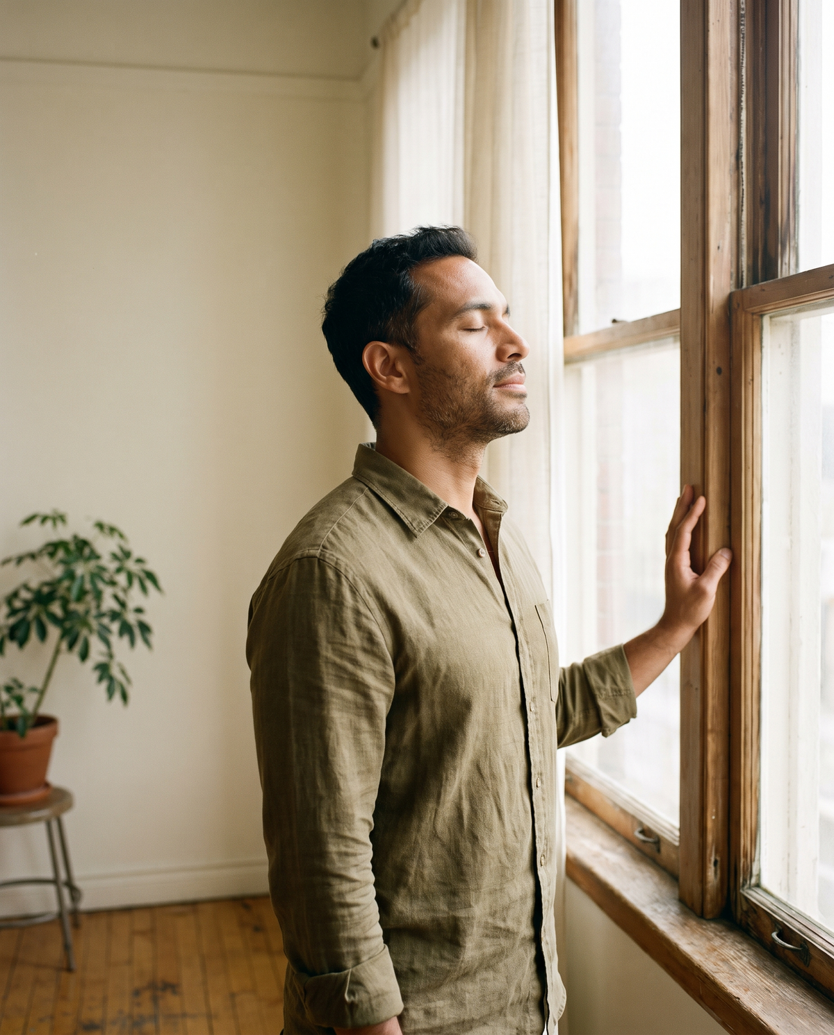 Man standing at a bright window taking a slow breath